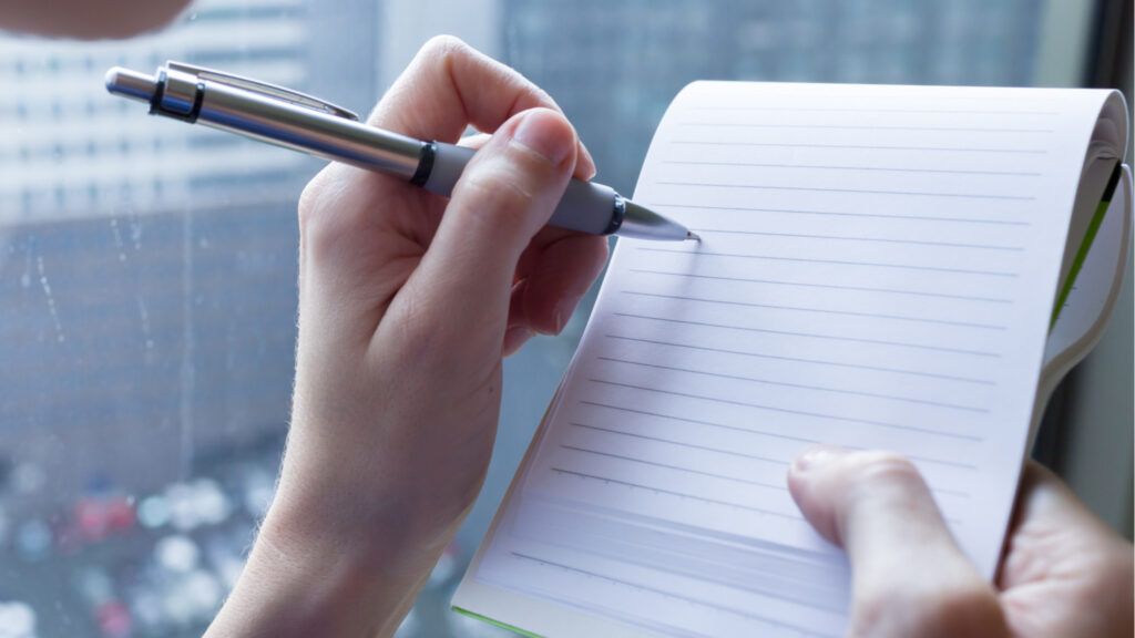 A landscape image of someone holding a pen to lined paper